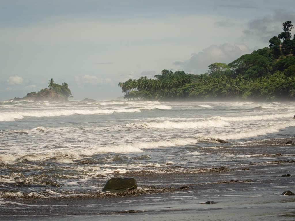 Dominicalito Beach in Costa Rica. White waves, grey sand, green jungle.