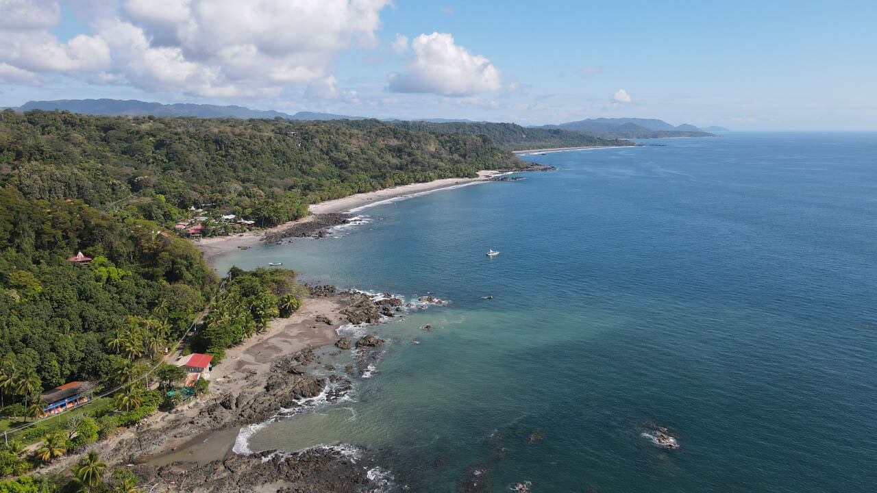 An aerial view of Montezuma, Costa Rica, showing the blue ocean, green forest covered hills and the town.