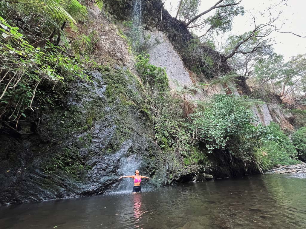 Woman, enjoying the cold trickle of the waterfall at Vandara on a dry sunny day.