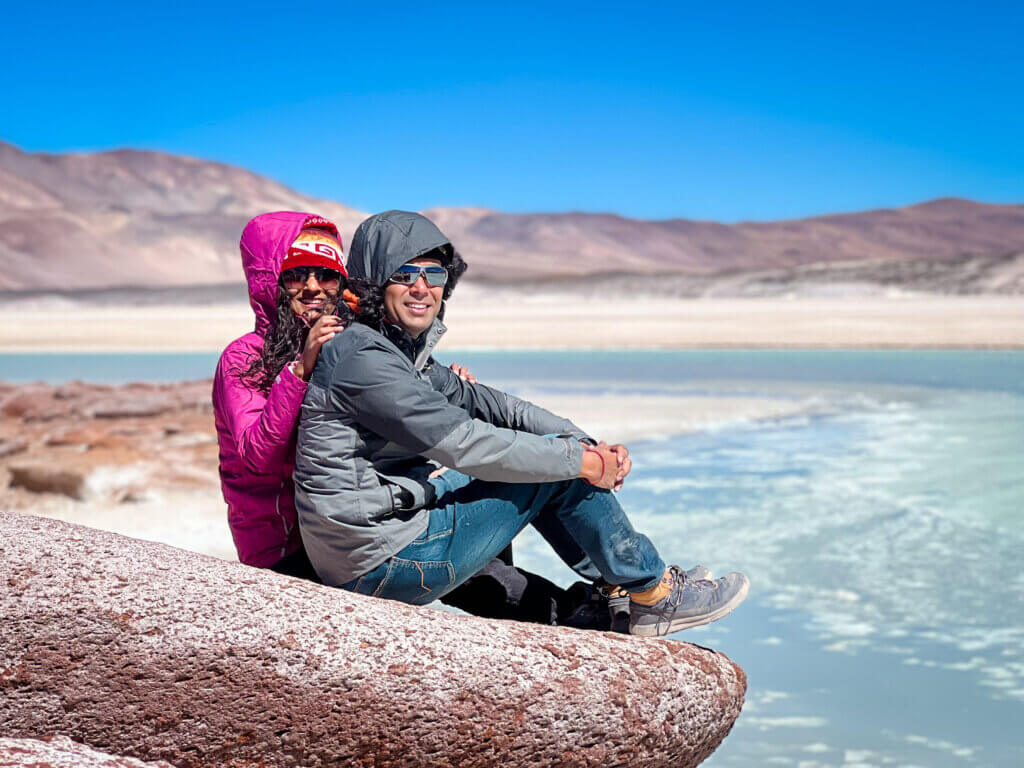 Couple seated on the edge of a rock facing the salt flat lake in Atacama region of Chile.