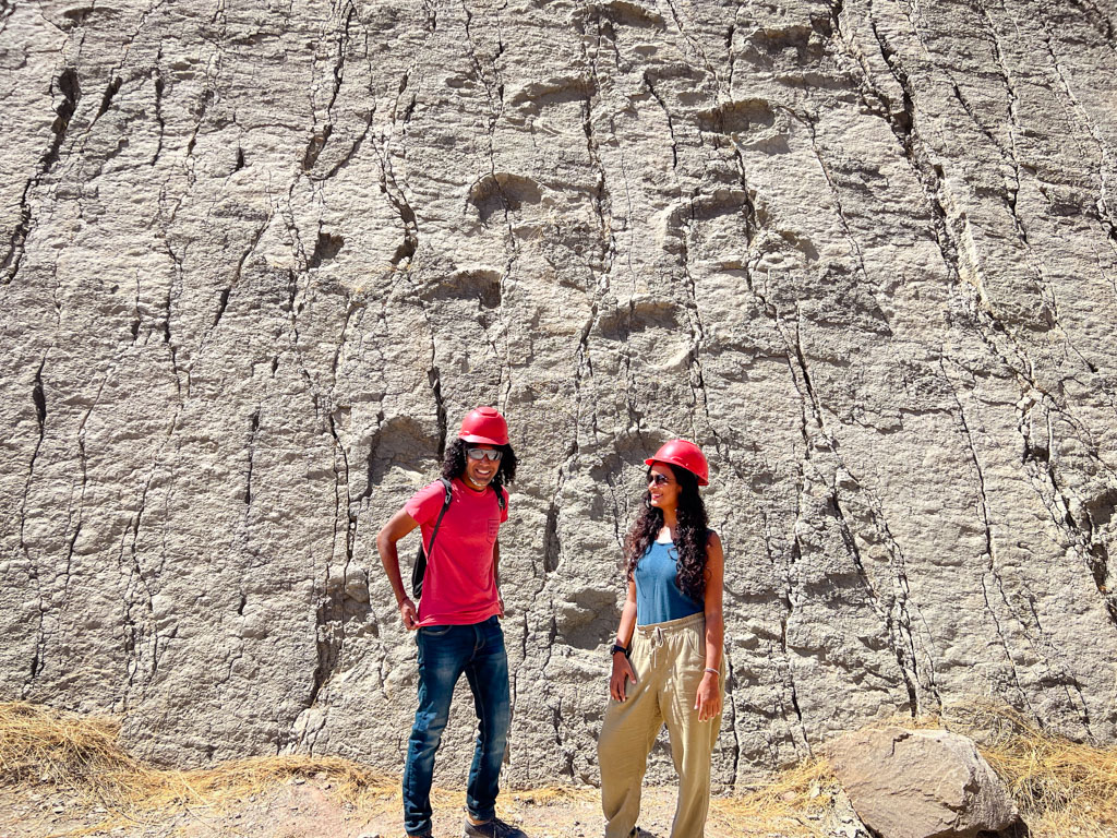 A man and a woman standing in front of a wall with real dinosaur footprints in Parque Cretacico, Sucre