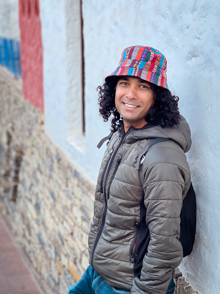 Man in jeans and jacket, wearing a hat, leaning against a wall in Sucre, Bolivia.