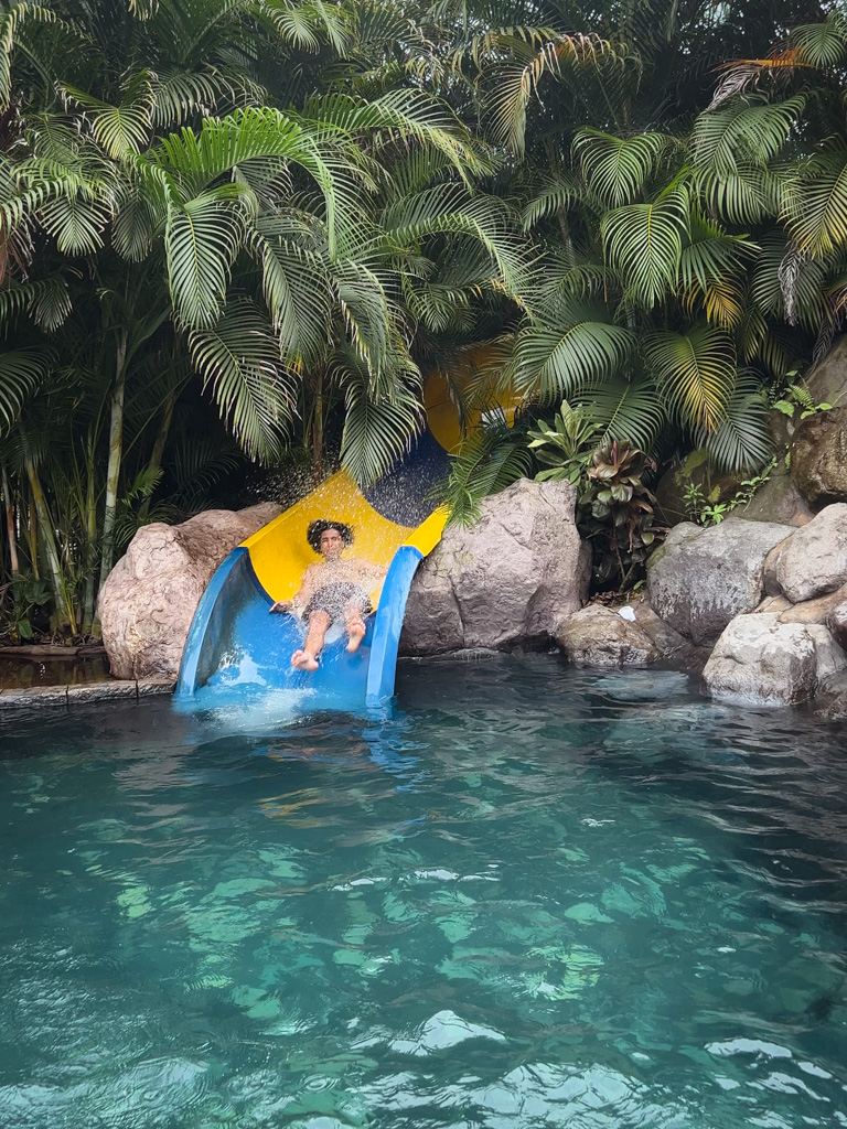 Man coming down the water slide, at the first thermal water pool of Relax Termalitas Hot Springs in La Fortuna, Costa Rica.