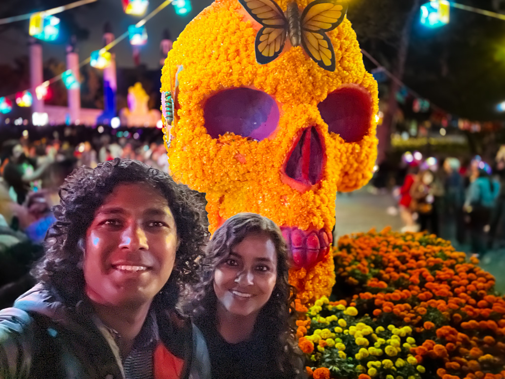 Couple posing before a huge skull made of marigold at Chapultepec Park, decked up in Day of the Dead special decorations.