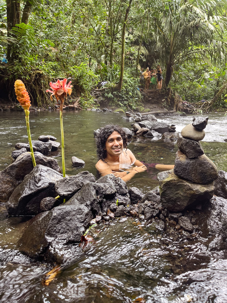 A man smiling, while sitting in El Choyin - the free hot springs of La Fortuna, Costa Rica.