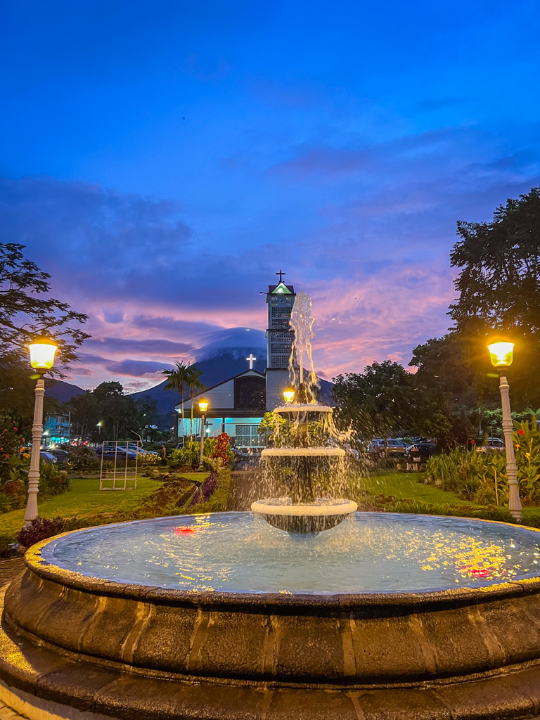 A Fountain lit by electric lamps with the La Fortuna town church and the Arenal Volcano in the background on an evening in the park of La Fortuna town center. It is one of the free thing to do in La Fortuna, Costa Rica.